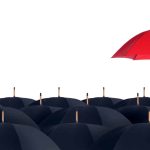 A red umbrella stands higher than a crowd of black umbrellas.