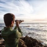 person with spyglass looks at ocean horizon